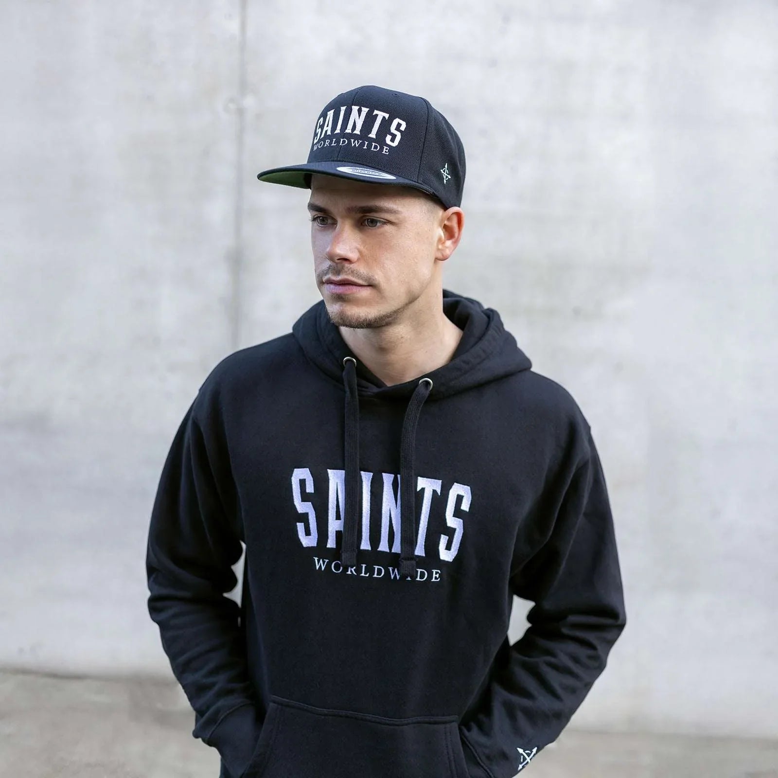 Model wearing full Saints Worldwide outfit, featuring hoodie and black embroidered snapback